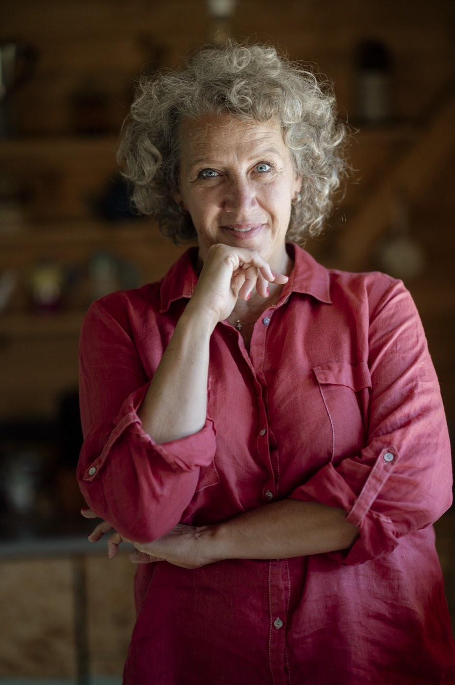 A modern portrait of a woman with curly hair smiling warmly in a warmly-lit interior.